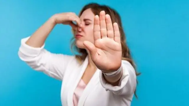 Жінка прикриває однією рукою ніс, а іншу направила на камеру