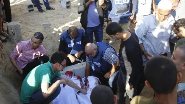 Al Jazeera journalist Wael Al-Dahdouh leans above the bodies of his family members as they are buried