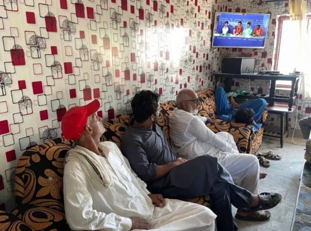 अरशद के गांव में टीवी पर उनकी प्रेसवार्ता देखते लोग