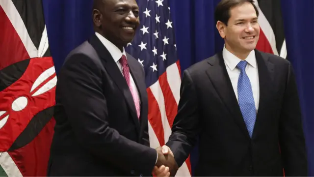 Marco Rubio (kulia) na Rais wa Kenya William Ruto (kushoto), wakiwa wamevalia suti nyeusi na tai, wakipeana mikono jijini New York mnamo Septemba 2025 mbele ya bendera za Kenya na Marekani.
.