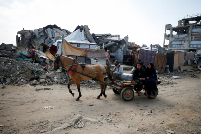 فلسطينيون يركبون عربة تجرها الخيول بين أنقاض المباني المدمرة