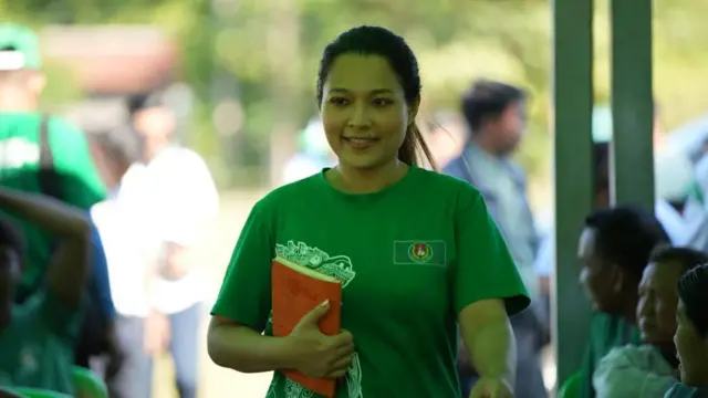 ဦးခင်ရီရဲ့ မဲဆွယ်ပွဲမှာတွေ့ရတဲ့ သမီးငယ်ဖြစ်သူ ဒေါ်မေဖူးပွင့်စိုး၊ ကြံ့ခိုင်ရေးပါတီတီရှပ် အစိမ်းရောင်ကိုဝတ်ဆင်ထားပြီး စာအုပ်တစ်အုပ်ကိုပိုက်ထားပါတယ်။