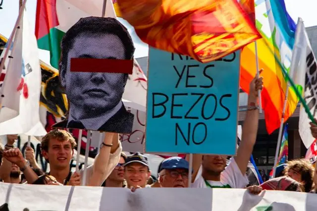 Öpücük evet bezos hayır yazılı bir posterin yanında gökkuşağı bayrakları ve Elon Musk'ın gözleri sansürlenen fotoğrafıyla protestocular. 