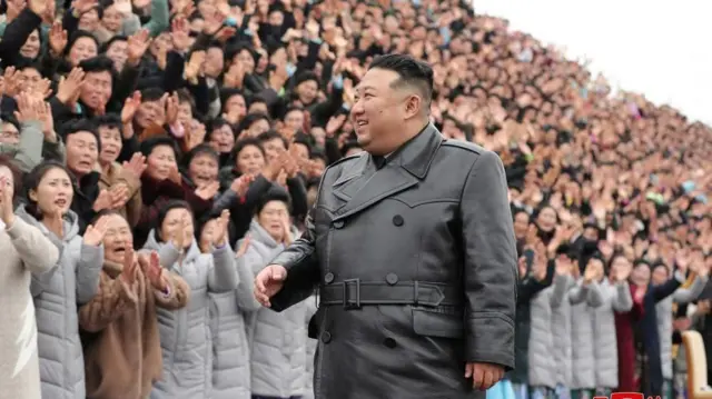 Kim Jong Un atambuka amwenyura imbere y'imbaga y'abantu imukomera amashyi