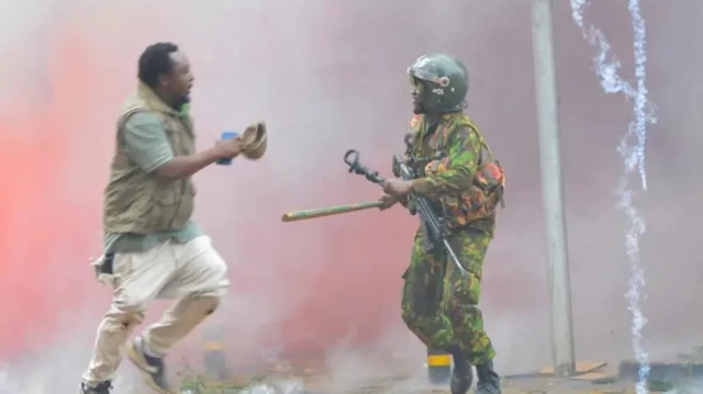 Umupolisi ahanganye n'umwe mu biyerekana, inyuma haboneka inkingi y' umwotsi (imyuka irakira) 