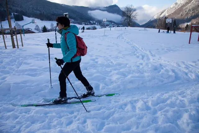 Жінка з коротким волоссям їде на лижах, навколо сніг і гори