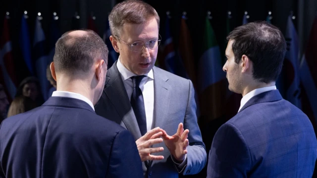 Сергій Корецький стоїть з двома чоловіками, спілкується з ними, жестикулюючи руками. 