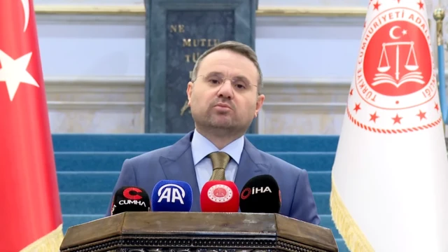 Adalet Bakanı Akın Gürlek konuşuyor. Boyu çok uzun değil, önünde dört mikrofon var.