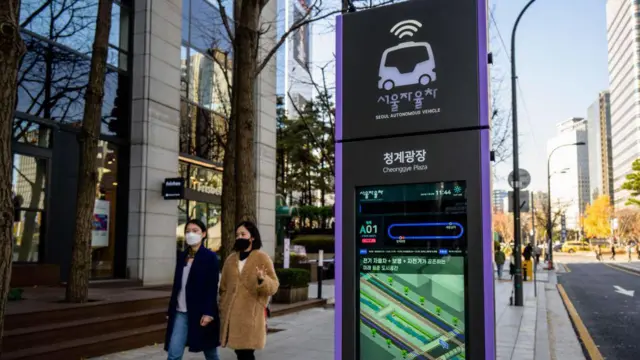 Pejalan kaki berjalan melewati tampilan informasi di halte yang ditunjuk untuk rute bus tanpa pengemudi pertama di Korea Selatan.