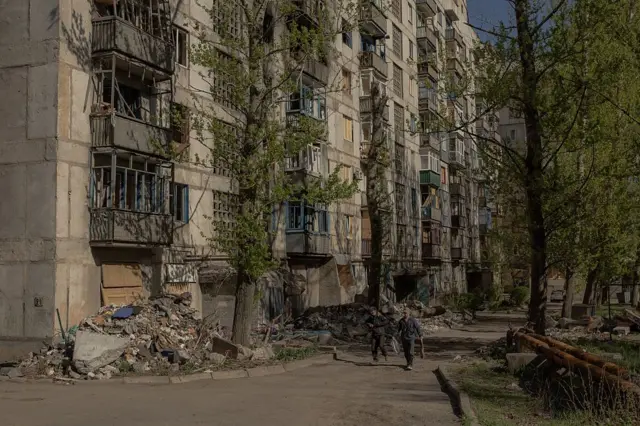 Donetsk bölgesinin doğusundaki Kostyantynivka'da hava saldırılarından ağır hasar gören konutların önünden geçen insanlar.