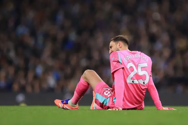 Gianluigi Donnarumma, vestido con su uniforme rosado, el apellido y el número 25 impresos en su espalda, está sentado en el cesped
