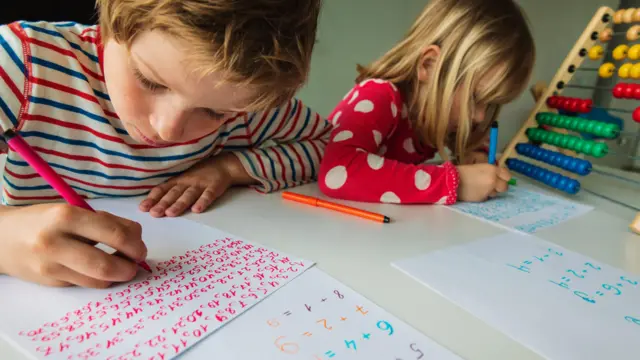 Kağıtlarına renkli kalemlerle yazılar yazan bir kız ve erkek çocuğu