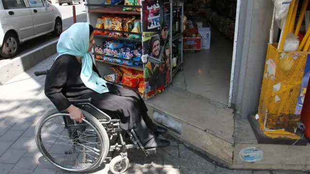 زنی سوار بر ویلچر جلوی پله در یک مغازه خواروبارفروشی در تهران