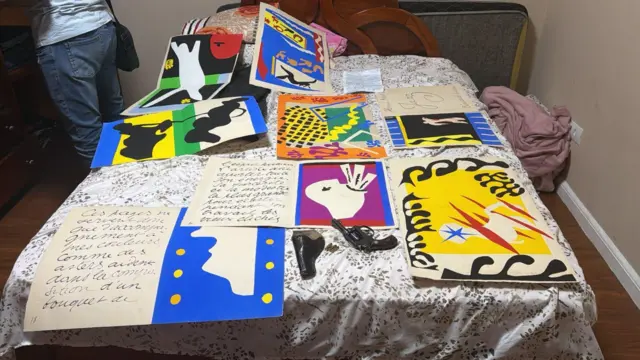 Las ilustraciones de Matisse, collages recortados en colores primarios y negro, se muestran colocadas en una cama, junto a una pistola