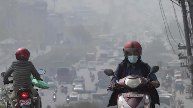 धुम्म परेको मौसममा मोटरसाइकलमा आवतजावत गरिरहेका व्यक्तिहरू
