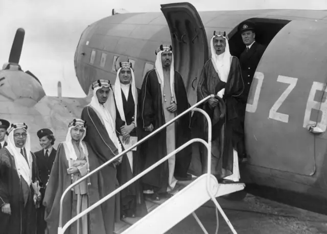 
صورة التقطت في أغسطس/آب عام 1945. وفيها خمسة من أبناء العاهل السعودي عبد العزيز بن سعود يستقلون طائرة في مطار بريطاني. وهم الأمير فيصل (لاحقا الملك فيصل)، والأمير محمد، والأمير فهد (لاحقا الملك فهد)، والأمير عبد الله الفيصل، والأمير نواف. وفي أقصى اليسار السفير السعودي في لندن.
