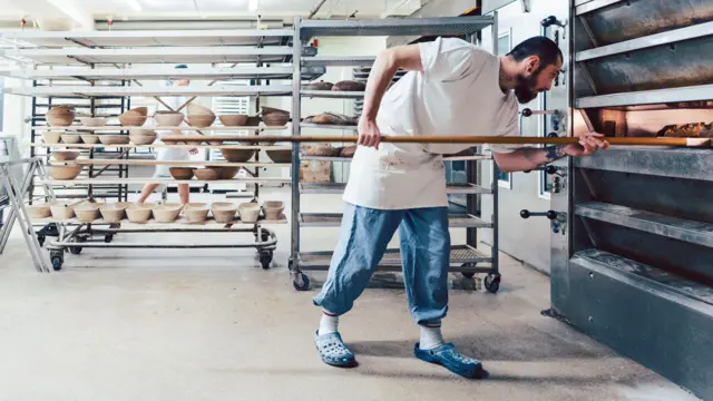 Un trabajador en una panadería de Alemania saca panes de un horno con una pala de madera