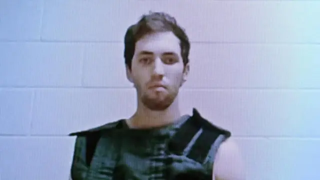 Foto policial de Tyler Robinson, acusado del asesinato del activista conservador Charlie Kirk, mirando serio a cámara, con un chaleco protector