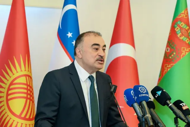 Memmedov bir kürsüde farklı bayrakların önünde konuşuyor. 