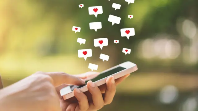 Крупний план руки, яка тримає смартфон із значком серця на тлі вулиці в парку