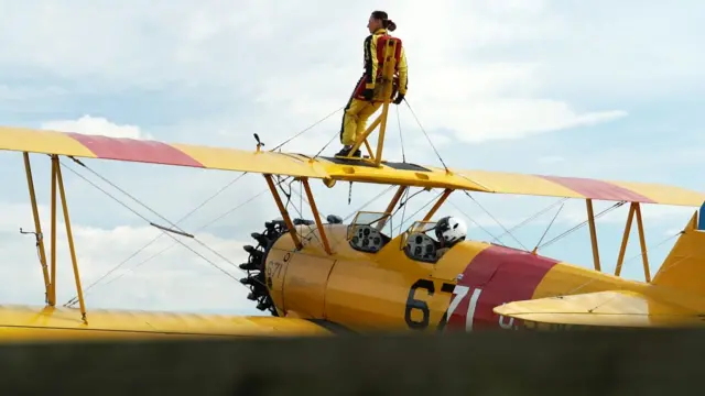 Dr Bernadette Hard dressed in a yellow jumpsuit standing on top of a yellow plane while taking part in a wing-walk