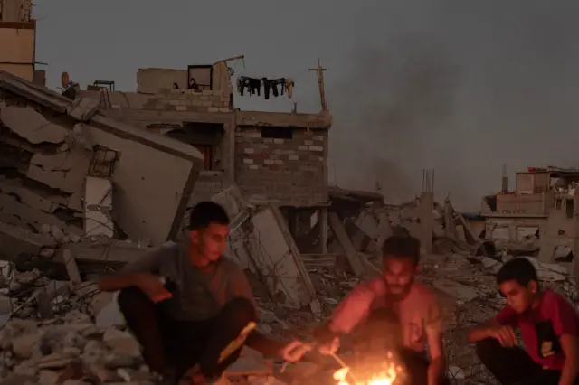 Palestinians sit next to a fire in the rubble of their destroyed home in Khan Younis 