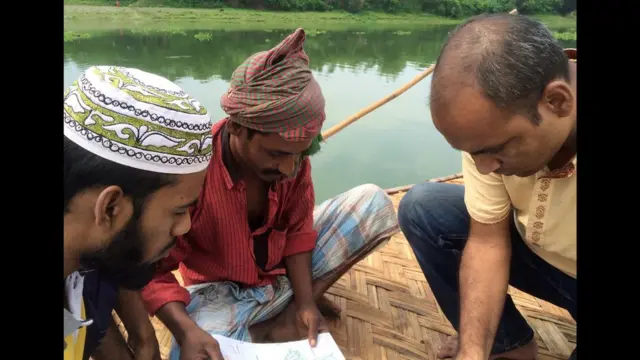 Três pessoasjogo slotbarco olhando para mapa Local villagers stare at a map while sitting on a boat