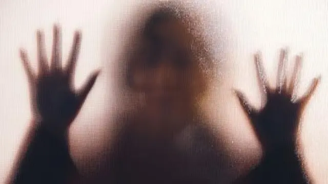 За дверима з непрозорим склом стоїть дівчина, вона впирається руками у скло.