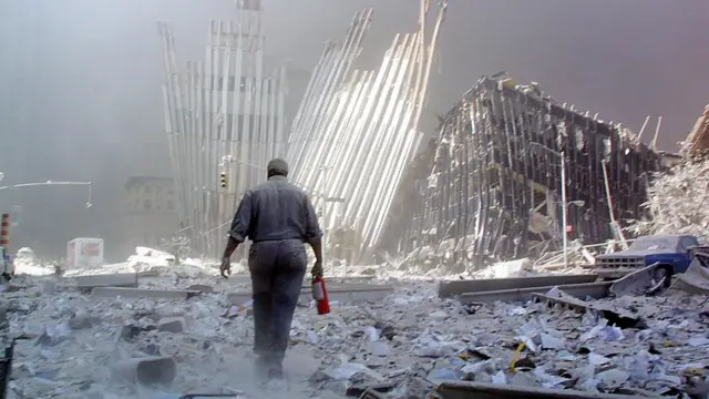 অগ্নিনর্বাপনী যন্ত্র নিয়ে ধ্বংসস্তুপের দিকে হেঁটে যাচ্ছেন এক ব্যক্তি