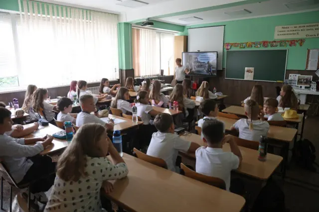 Діти сидять за партами у школі. 