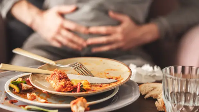 Pessoa com as mãos no estômago com vários pratos sujos vazios empilhados