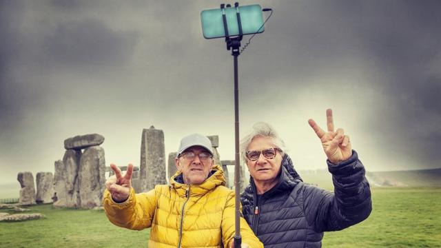 Dos hombres maduros, posando y tomando un selfie en el sitio arqueológico de Stonehenge, Reino Unido.