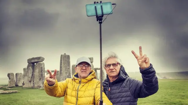 Dos hombres maduros, posando y tomando un selfie en el sitio arqueológico de Stonehenge, Reino Unido.
