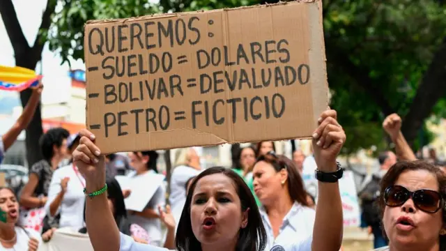 Manifestante segura placa que diz: 'Queremos: Salário = Dólares; Bolívar = Desvalorizado; Petróleo = Fictício'