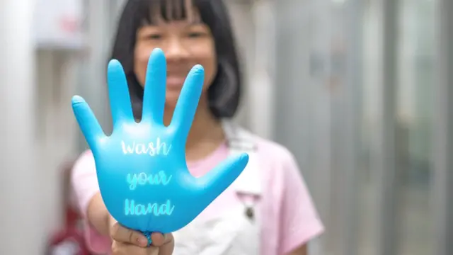 Una mujer sostiene un guante con la frase "lávate las manos" en inglés.