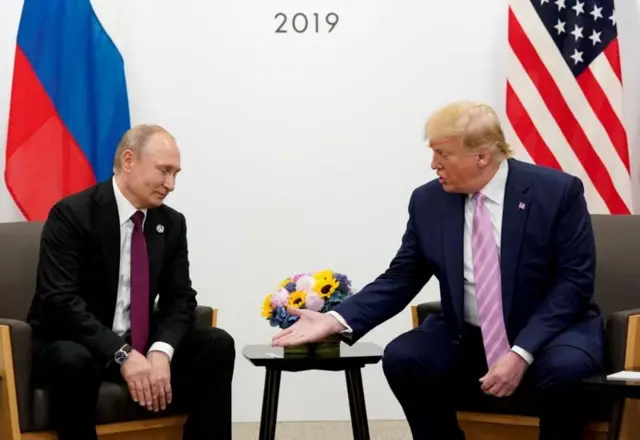 Putin e Trump sentados diante de bandeiras de seus respectivos países