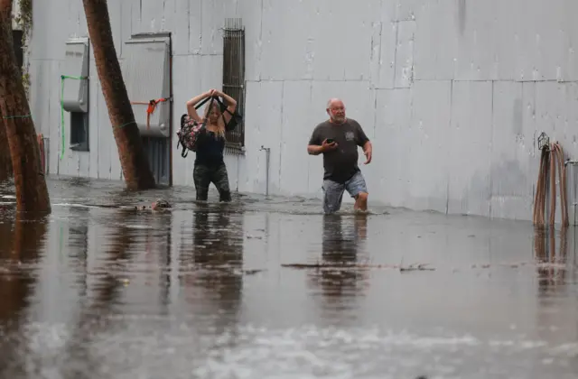 Gente camina a través de las inundaciones provocadas por el huracán Idalia después de su paso por la costa de Tarpon Springs, Florida.