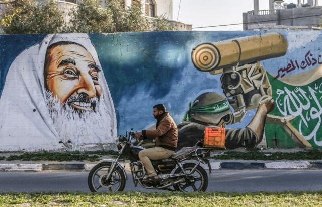 Motocicleta passa por um mural que retrata o falecido líder espiritual do Hamas, Sheikh Ahmed Yassin, sorrindo