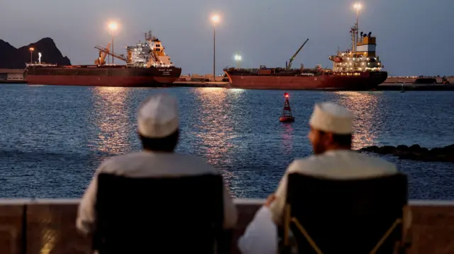 Dois homens diante de petroleiros atracados em Mascate