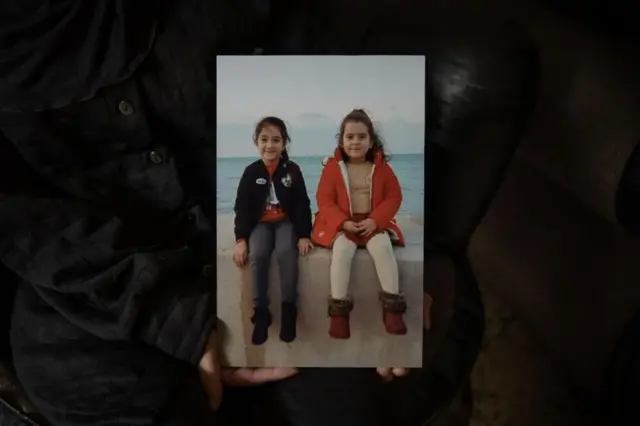 Rihab segurando uma foto das filhas, Tia e Naya, tirada durante um passeiologin betmotionBeirute — as meninas estão sentadaslogin betmotionum muro à beira-mar