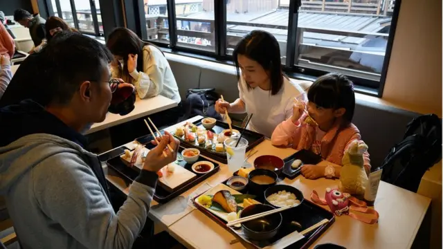 Visitors from Hong Kong dine at Edo Tsujiya seafood restaurant inside Toyosu Senkyaku Banrai retail complex in Tokyo, Japan, on Monday, Feb. 19. 2024. Booming numbers of foreign visitors to Japan are driving up prices at restaurants near tourist spots, as a weaker yen makes the country a bargain destination and local wages struggle to keep up with a broader rise in costs. Photographer: Akio Kon/Bloomberg via Getty Images