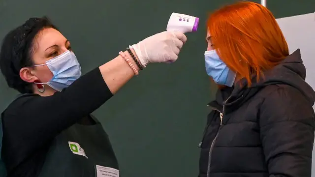 Член избирательной комиссии проверяет температуру у женщины на избирательном участке в Тбилиси 21 ноября 2020 года