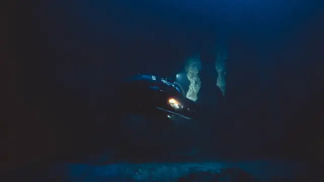 Submarino investiga as profundezas do Buraco Azul de Belize - imagem é toda escura, só é possível ver a luz do submarino iluminando pedaços de estalactites e refletindo de volta no equipamento
