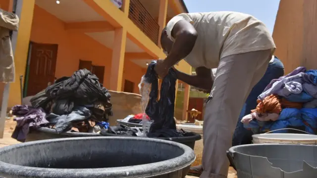 Wani mai sana'ar wanki da guga kenan a bakin aiki da tarin kaya a gabansa