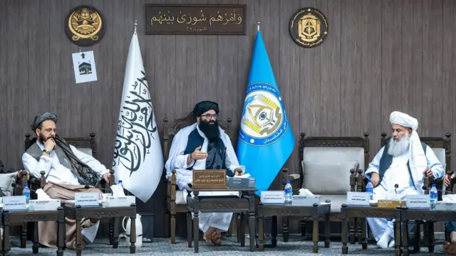 سراج الدین حقانی وزیر داخله در وسط و دو نفر با لباس سفید در دو طرف نشستهاند