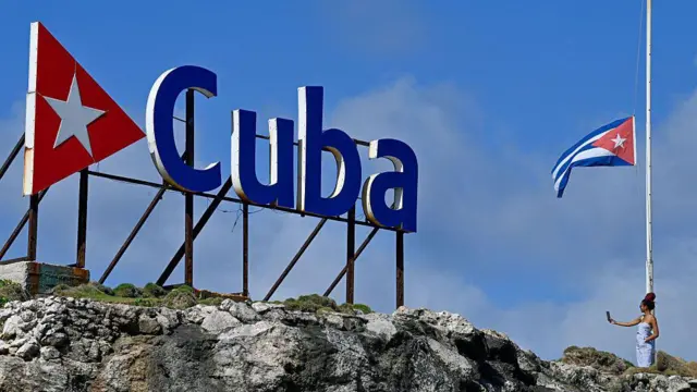 سائحة تلتقط صورة سيلفي وهي تقف بجوار العلم الكوبي المنكّس في هافانا في 5 يناير/كانون الثاني 2026.