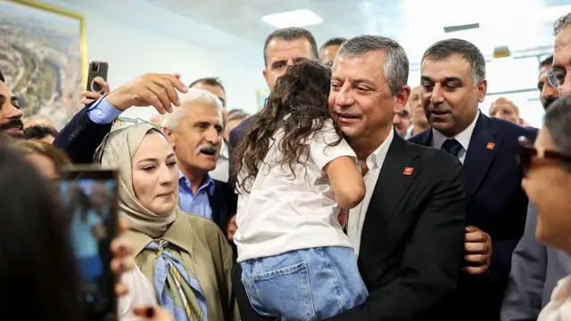 Özgür Özel'in 26 Haziran'da ziyaret ettiği Diyarbakır'da havalimanındaki karşılamadan bir fotoğraf. Kucağında sırtı dönük bir kız çocuk var. etrafı kalabalık. 