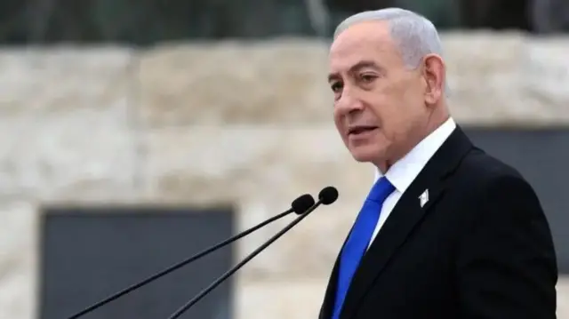Foro of Benjamin Natanyahu as e dey tok for microphone, e wear black coat, blue tie and white inner shirt.