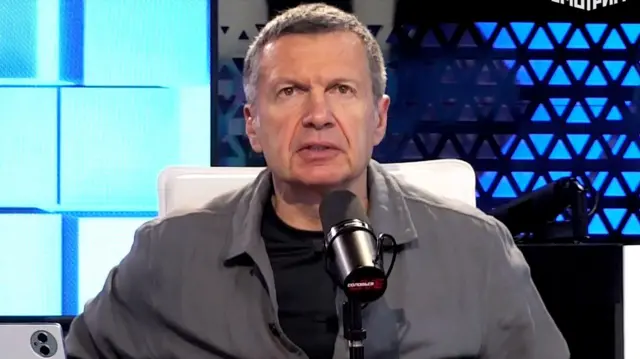 El presentador ruso Vladímir Solovyov sentado con un micrófono delante en el estudio de su programa. 