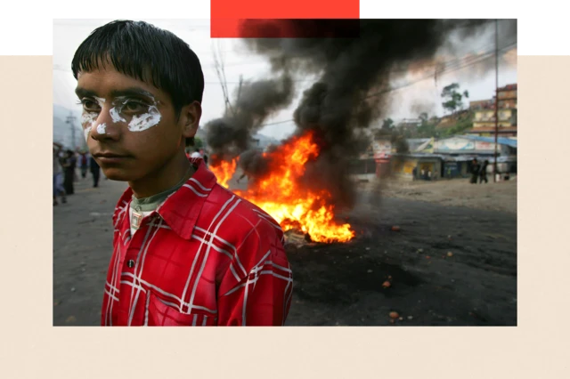 Mwandamanaji wa Nepal akiwa na dawa ya meno usoni mwake iliyotumika kukabiliana na gesi ya kutoa machozi akisimama karibu na moto wakati wa maandamano ya kupinga utawala wa kifalme wa njia ya King Gyanedra